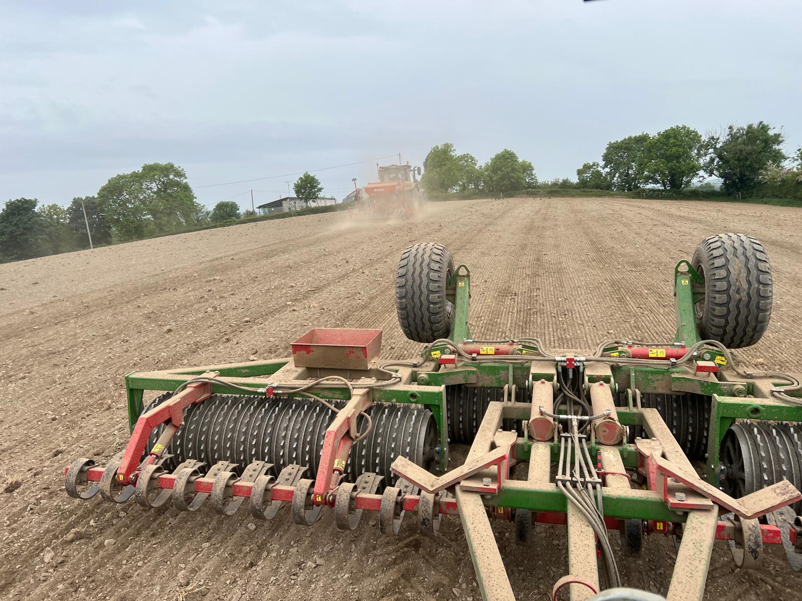 Land preparation equipment tilling soil in field with tractor in distance