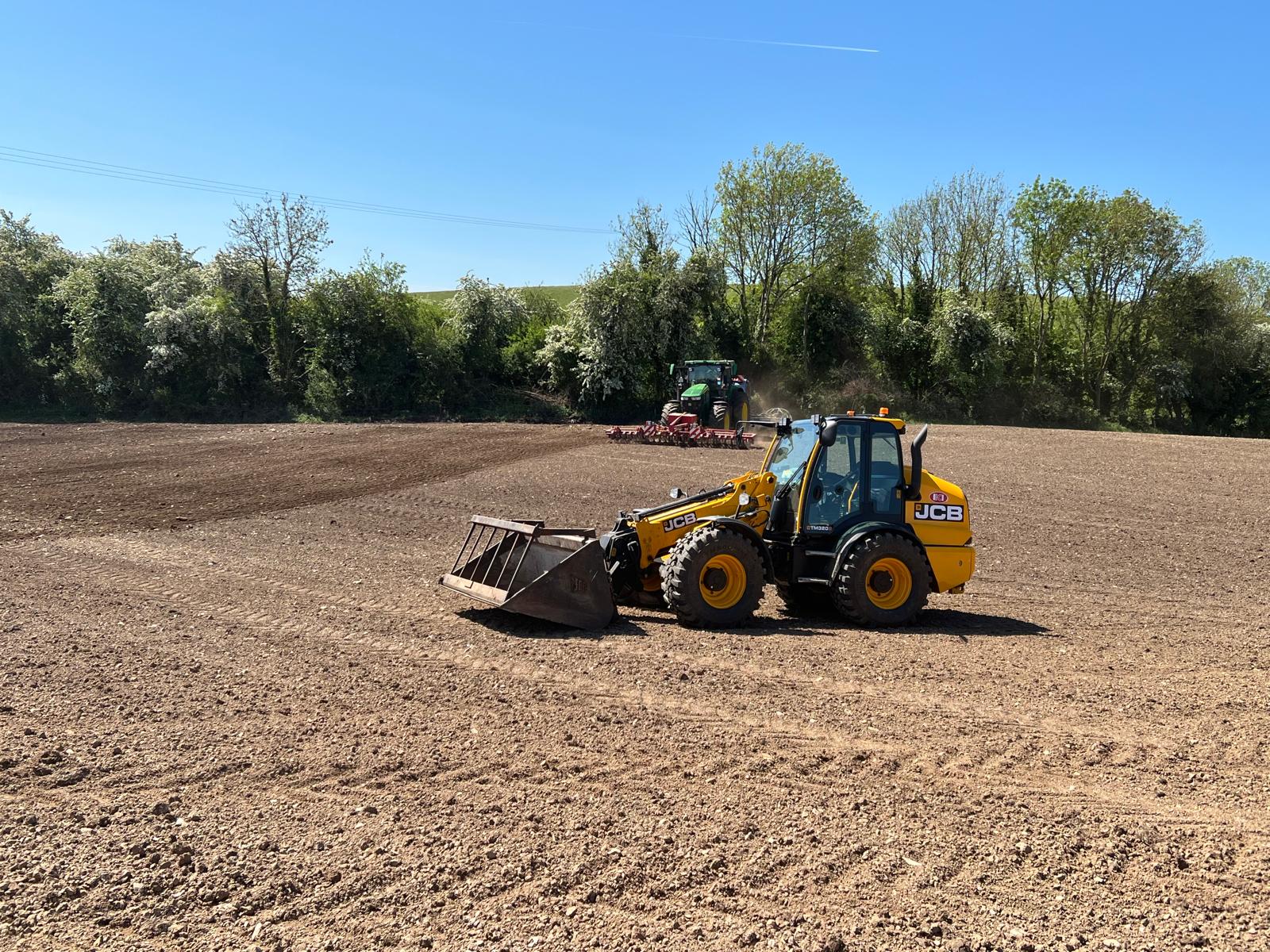 JCB loader and tractor working in open field preparing seedbed