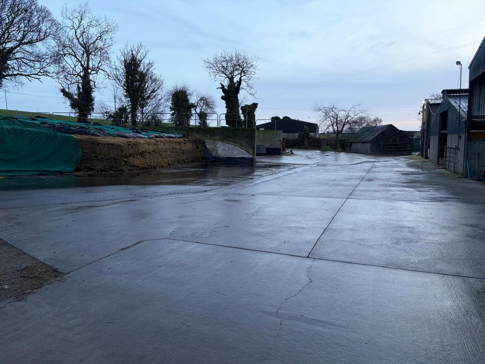 Clean concrete farmyard apron beside silage pit and farm sheds